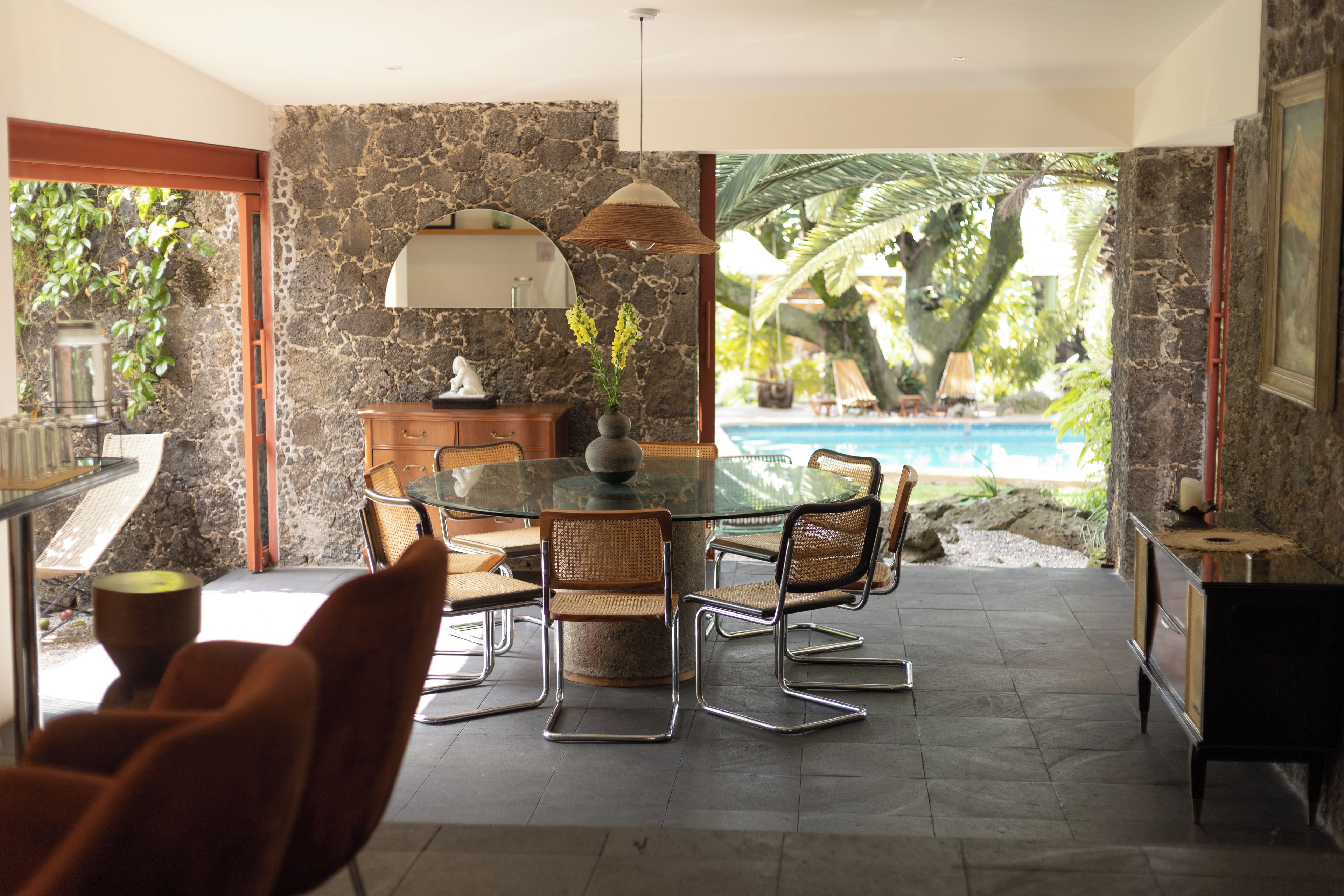 Un coin repas avec une table et des chaises en verre, un mur en pierre et une vue sur une piscine.