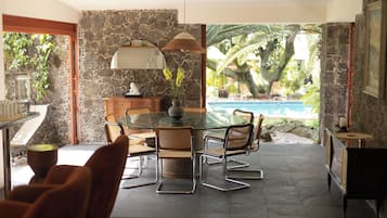 Un coin repas avec une table et des chaises en verre, un mur en pierre et une vue sur une piscine.