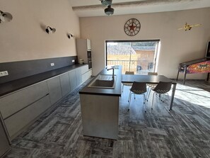 Una cocina moderna con una isla central, un comedor con sillas, un ventanal grande y un ventilador de techo.