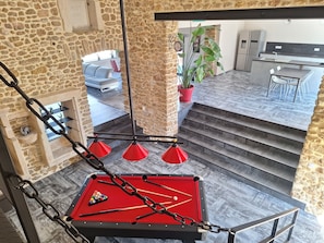 Ein Billardtisch mit roter Spielfläche, eine Uhr und ein Blumentopf in einem Raum mit Steinwänden und einer Treppe.