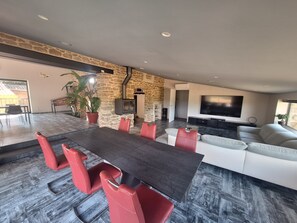 Ein modernes Wohnzimmer mit Steinwand, großem Flachbildfernseher, Kamin und Essbereich mit roten Stühlen.