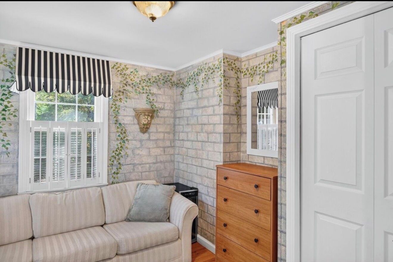 Una habitación con pared de ladrillo, ventana con contraventanas, sofá, cómoda y espejo.