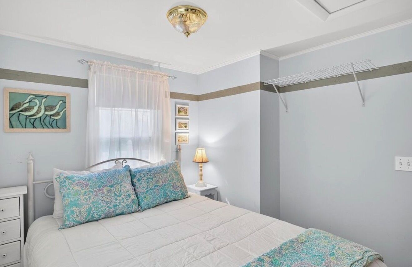 A bedroom with a bed, a bedside table with a lamp, a wall-mounted shelf, and a ceiling fan.