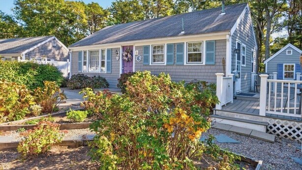 A single-story house with a front porch, a small deck, and a garden area with various plants. - Relaxing Cape Cod Cottage Getaway (Dennis)