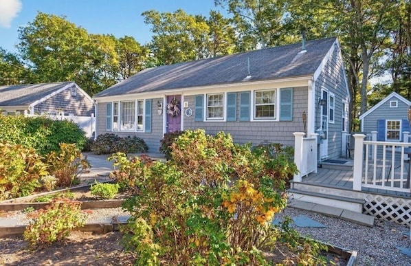 A single-story house with a front porch, a small deck, and a garden area with various plants.