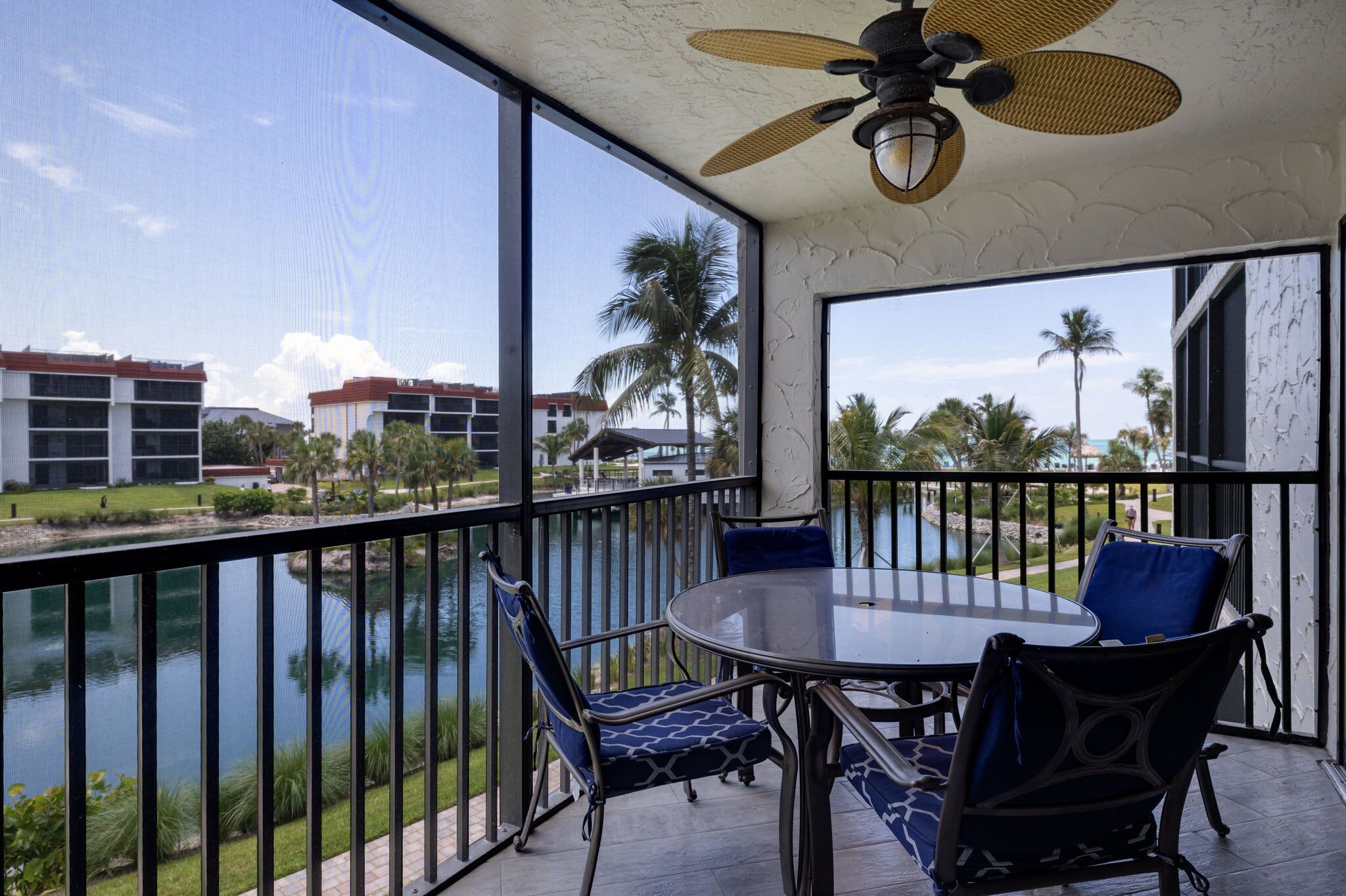 A balcony with a table and chairs, a view of a body of water, and palm trees.