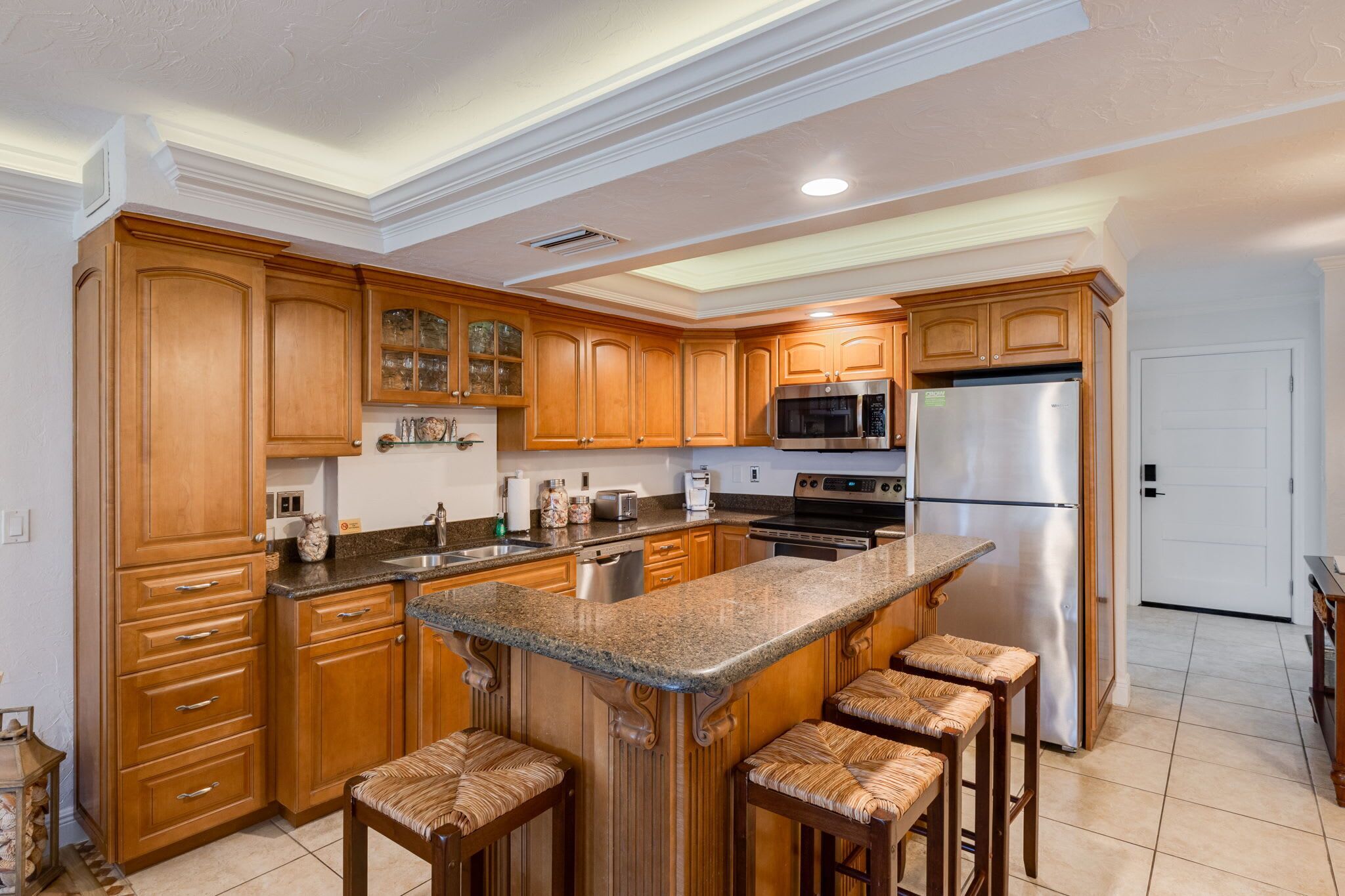 A kitchen with wooden cabinets, granite countertops, a stainless steel refrigerator, and a built-in island with bar stools.