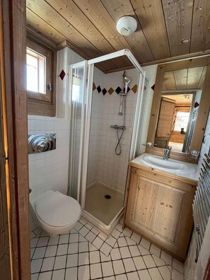 Ein kleines Badezimmer mit Dusche, Toilette und Waschbecken, mit Holzboden und Fliesen.