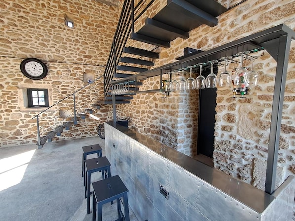 A stone-walled bar area with a clock, bar stools, and a staircase.