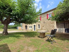 A stone building with red shutters, a tree in the foreground, and a stone bench. - Apartment 'Chez Vero & David - Piscine' with Private Pool, Wi-Fi and Air Conditioning (Suze-la-Rousse)
