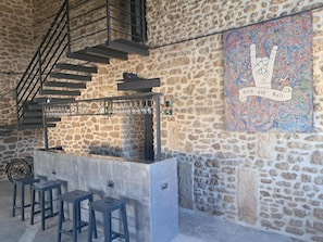 A bar area with stools, a bar counter, and a staircase against a stone wall. - Apartment 'Chez Vero & David - Piscine' with Private Pool, Wi-Fi and Air Conditioning (Suze-la-Rousse)