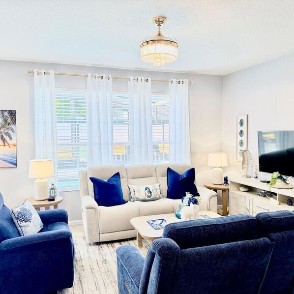 Ein Wohnzimmer mit einer Couch, zwei Sesseln, einem Couchtisch, einem Fernseher und einer Deckenleuchte.