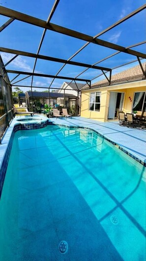 Ein klares, blaues Schwimmbecken mit Glasumrandung, umgeben von einer Terrasse mit Stühlen und Sonnenschutz.