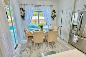 Ein Essbereich mit Tisch für vier Personen, einem Kühlschrank und Blick auf einen Swimmingpool.