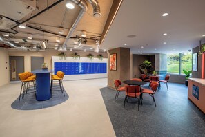 A modern office space with a blue conference table, orange chairs, a black round table, and a reception area with a plant. - Ironworks House (London)