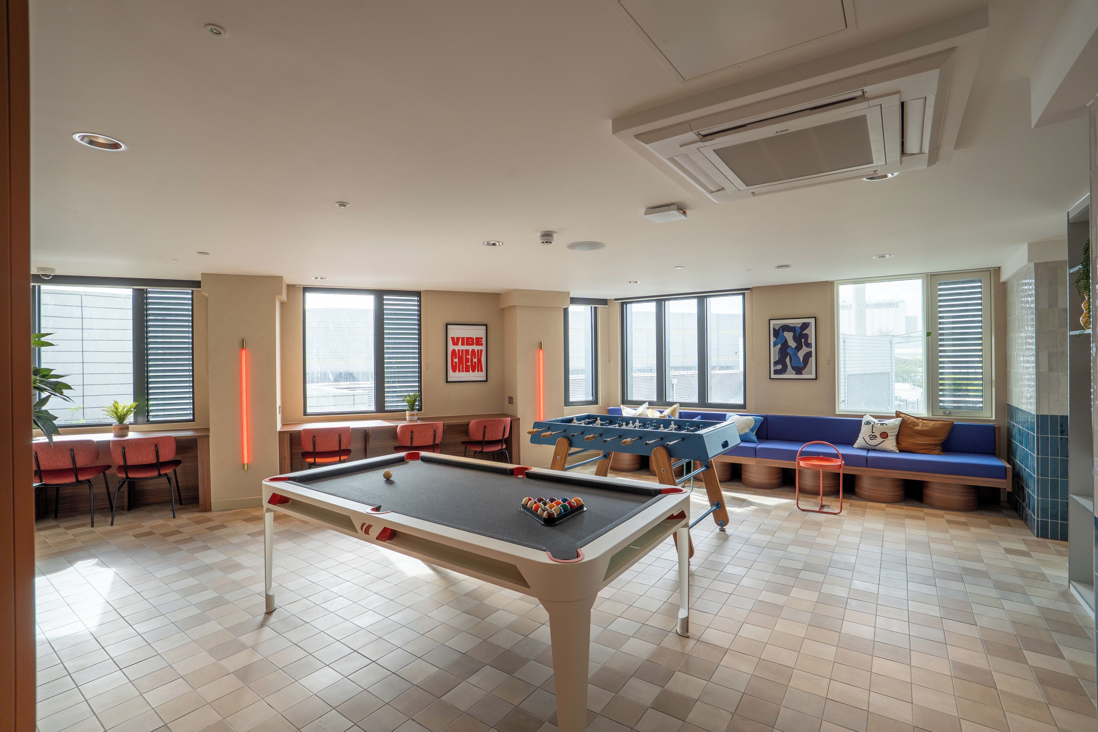 A pool table in a room with large windows, a sofa, and a foosball table.