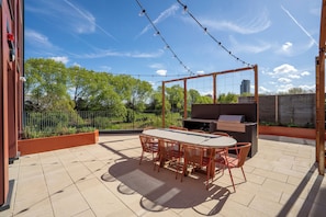An outdoor patio with a table and chairs, a grill, and a view of trees and buildings. - Ironworks House (London)