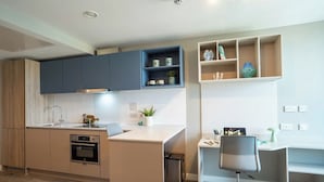Une cuisine moderne dotée d’appareils électroménagers intégrés, un coin repas avec une table et des chaises blanches, et un petit espace bureau avec un bureau et une chaise.
