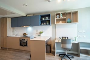 A modern kitchen with built-in appliances, a dining area with a white table and chair, and a small office space with a desk and chair. - Ironworks House (London)