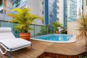 A rooftop pool area with lounge chairs, potted plants, and a view of surrounding buildings. - Apto de luxo com piscina privativa e vista mar (Balneário Camboriú)