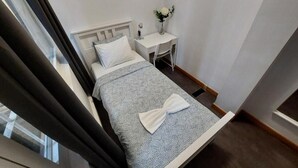 Un dormitorio con cama, una mesita de noche con un florero y una ventana con cortinas.