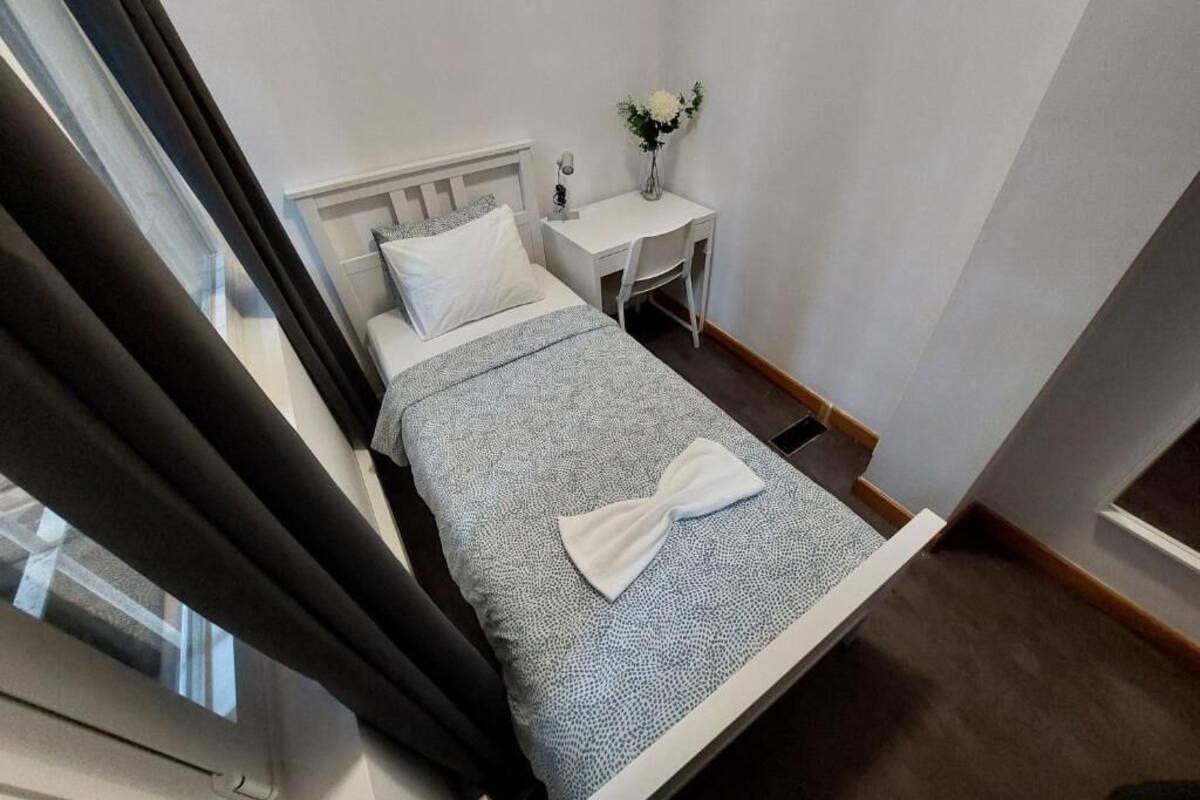 Un dormitorio con cama, una mesita de noche con un florero y una ventana con cortinas.