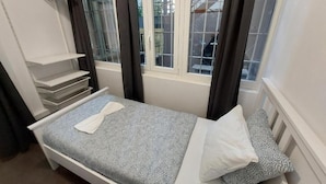 Una habitación pequeña con cama individual, ventana, ropa de cama blanca y toalla blanca.