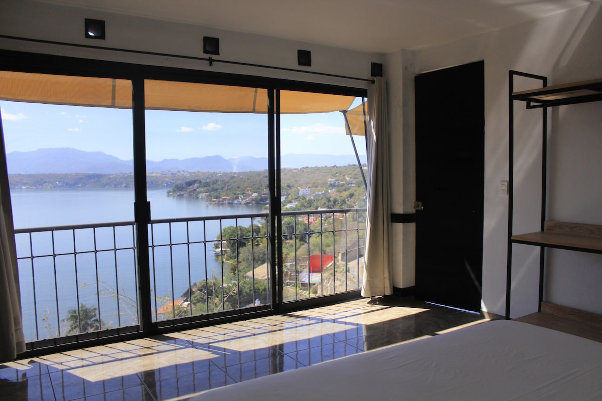 A room with a large window overlooking a body of water and a mountainous landscape.