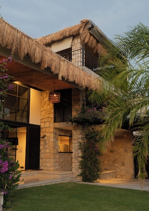 A two-story house with a stone facade, a thatched roof, and a balcony with a railing.