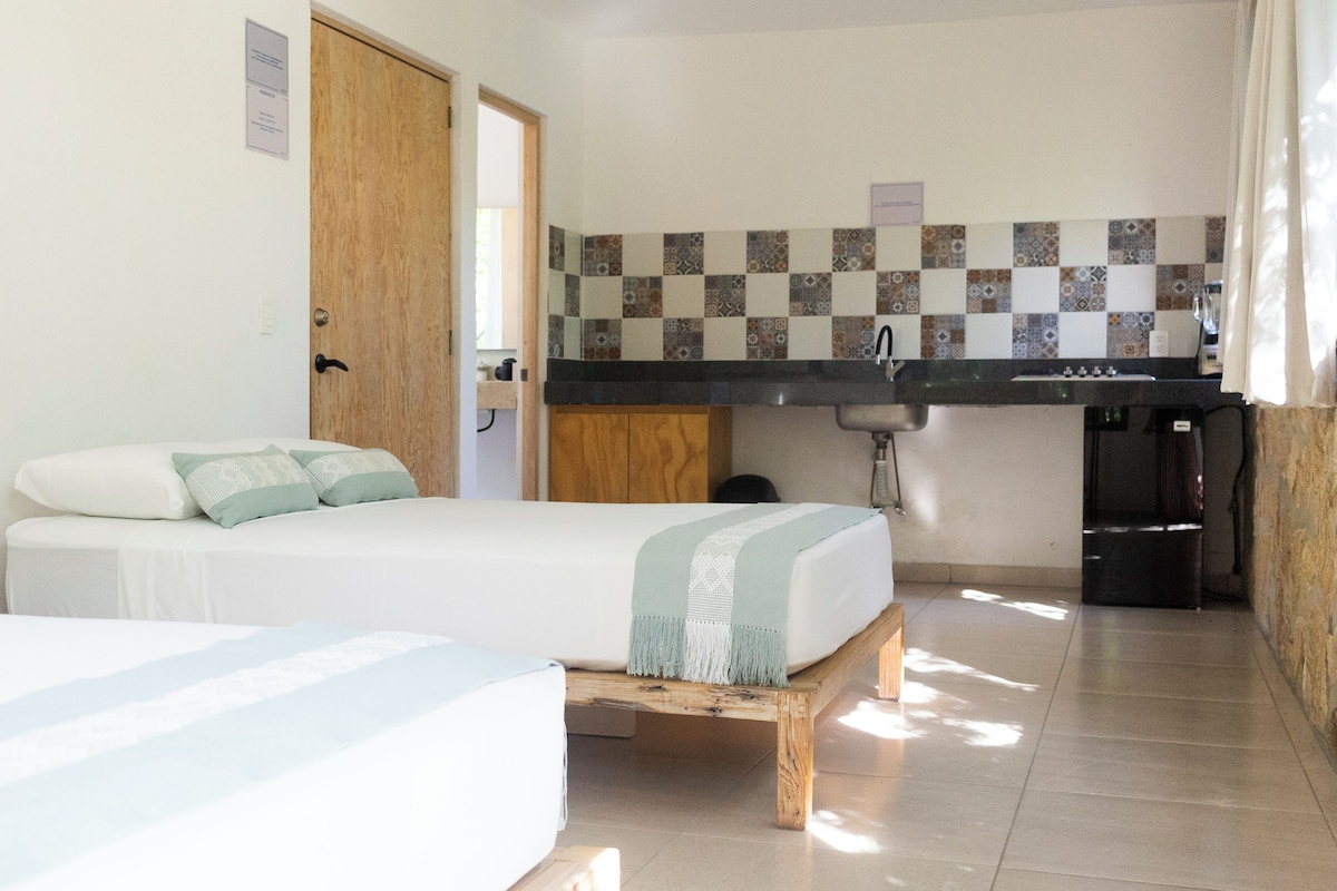 Quarto com cama, pequeno espaço de cozinha e porta do banheiro.