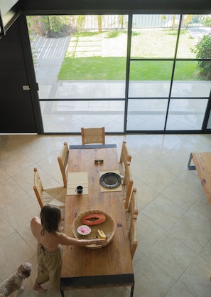 An open-plan living space with a dining table, chairs, and a view through large glass doors to an outdoor area.