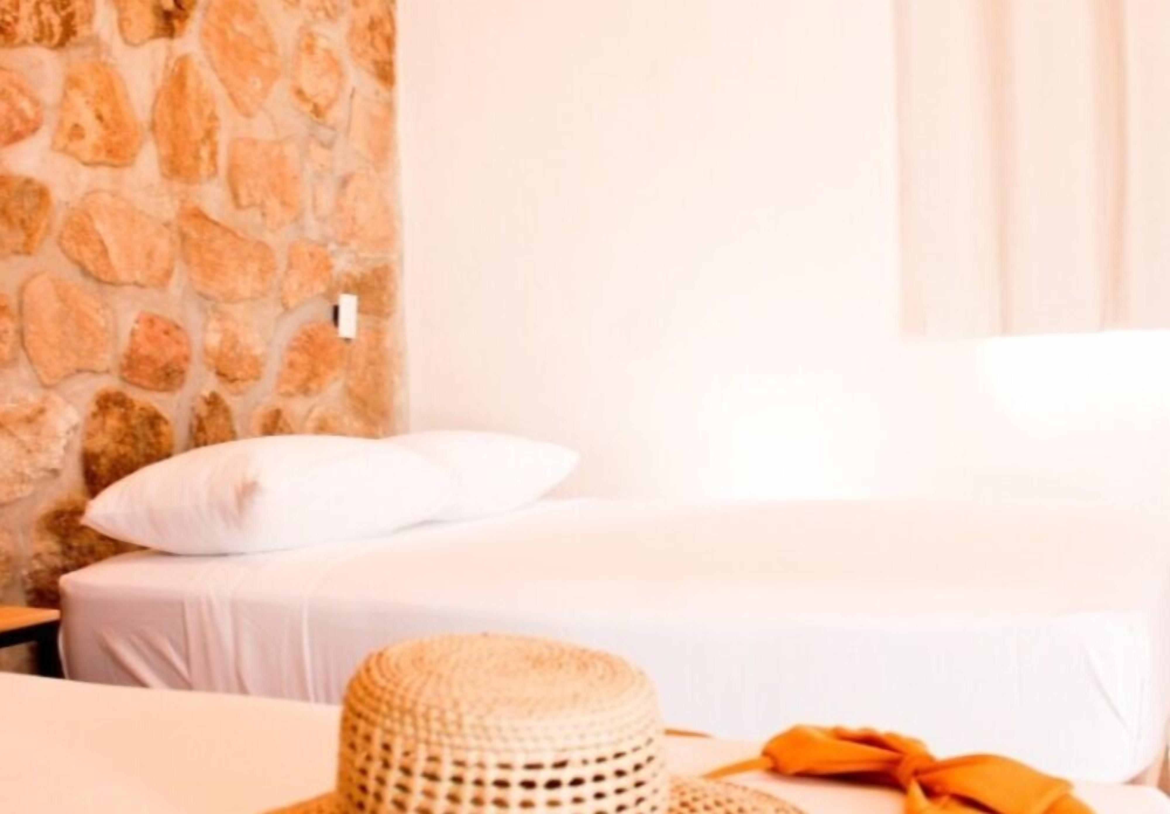 Una habitación con pared de piedra, una cama con ropa blanca y una cesta tejida.