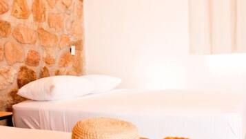 Una habitación con pared de piedra, una cama con ropa blanca y una cesta tejida.