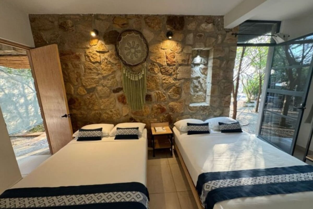Quarto com duas camas, parede de pedra, mesa de cabeceira e janela com vista.