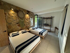 Un dormitorio con dos camas, una pared de piedra, decoración colgante y cabina de ducha de vidrio.