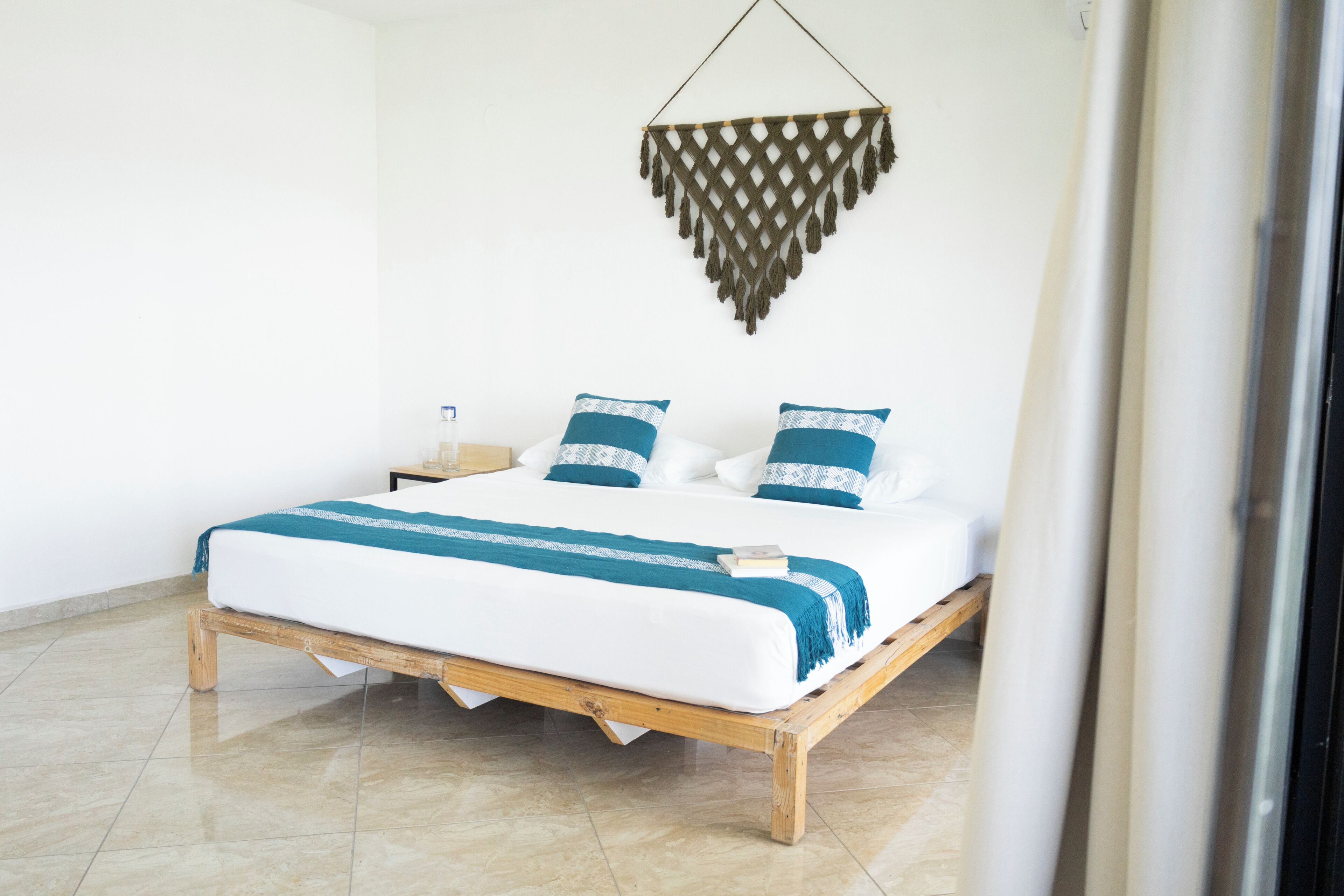Una cama con estructura de madera, ropa de cama blanca y almohadas con estampado azul y blanco.