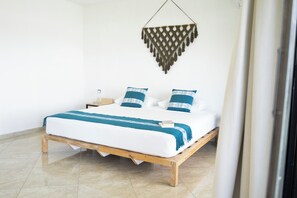 Una cama con estructura de madera, ropa de cama blanca y almohadas con estampado azul y blanco.