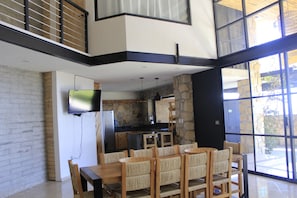 Uma cozinha moderna com painel de pedra, uma área de jantar com mesa e cadeiras de madeira, e uma TV de tela plana fixada na parede.