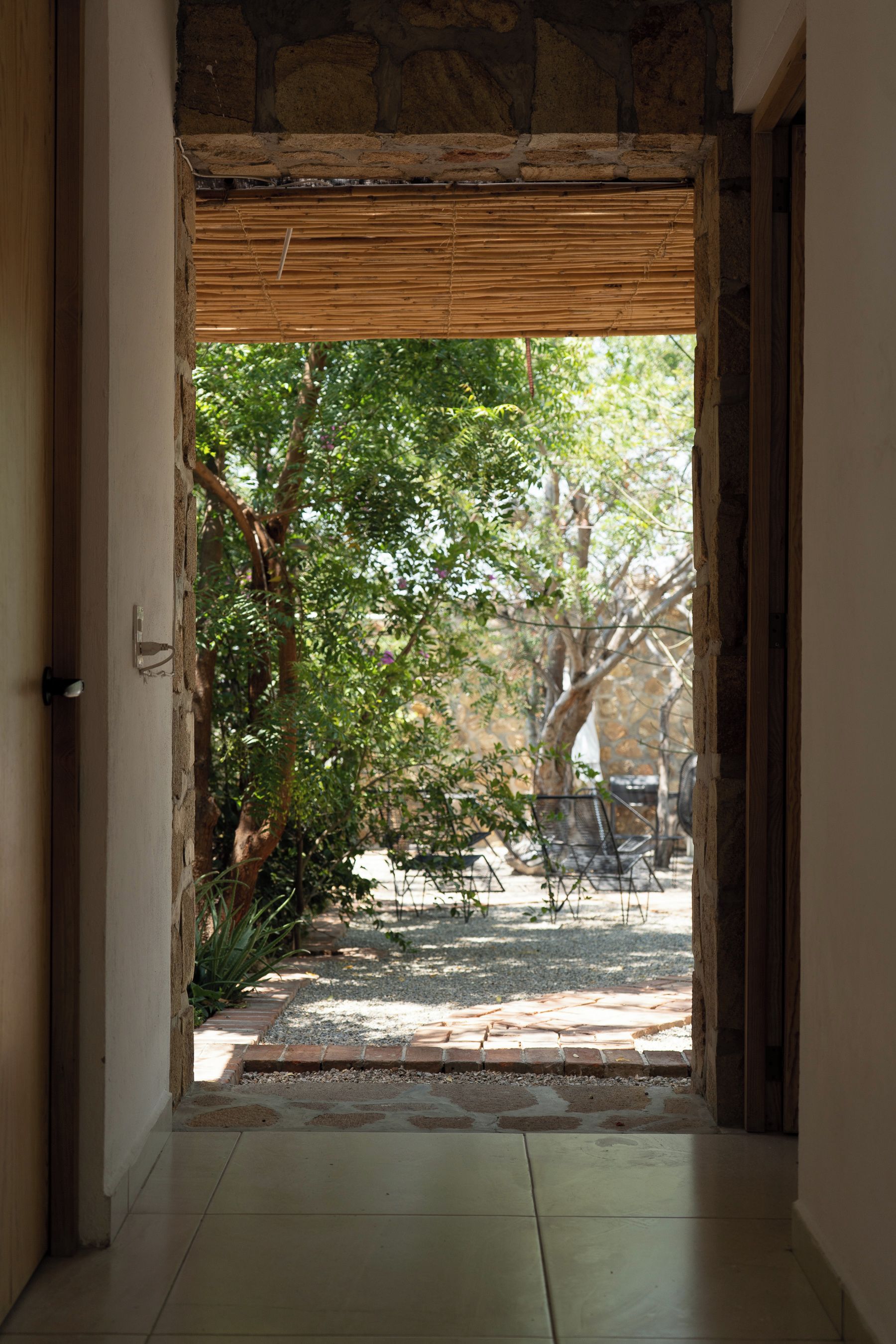 A doorway leading to an outdoor area with a stone wall, a bamboo blind, and a garden with trees and a patio.