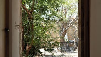 A doorway leading to an outdoor area with a stone wall, a bamboo blind, and a garden with trees and a patio.