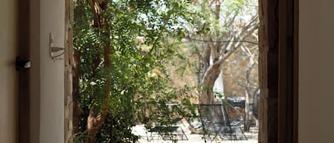 A doorway leading to an outdoor area with a stone wall, a bamboo blind, and a garden with trees and a patio.