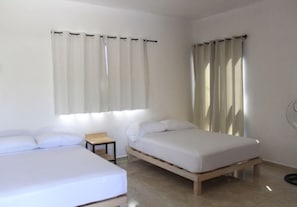 Quarto com duas camas, uma mesinha e uma janela com cortinas.