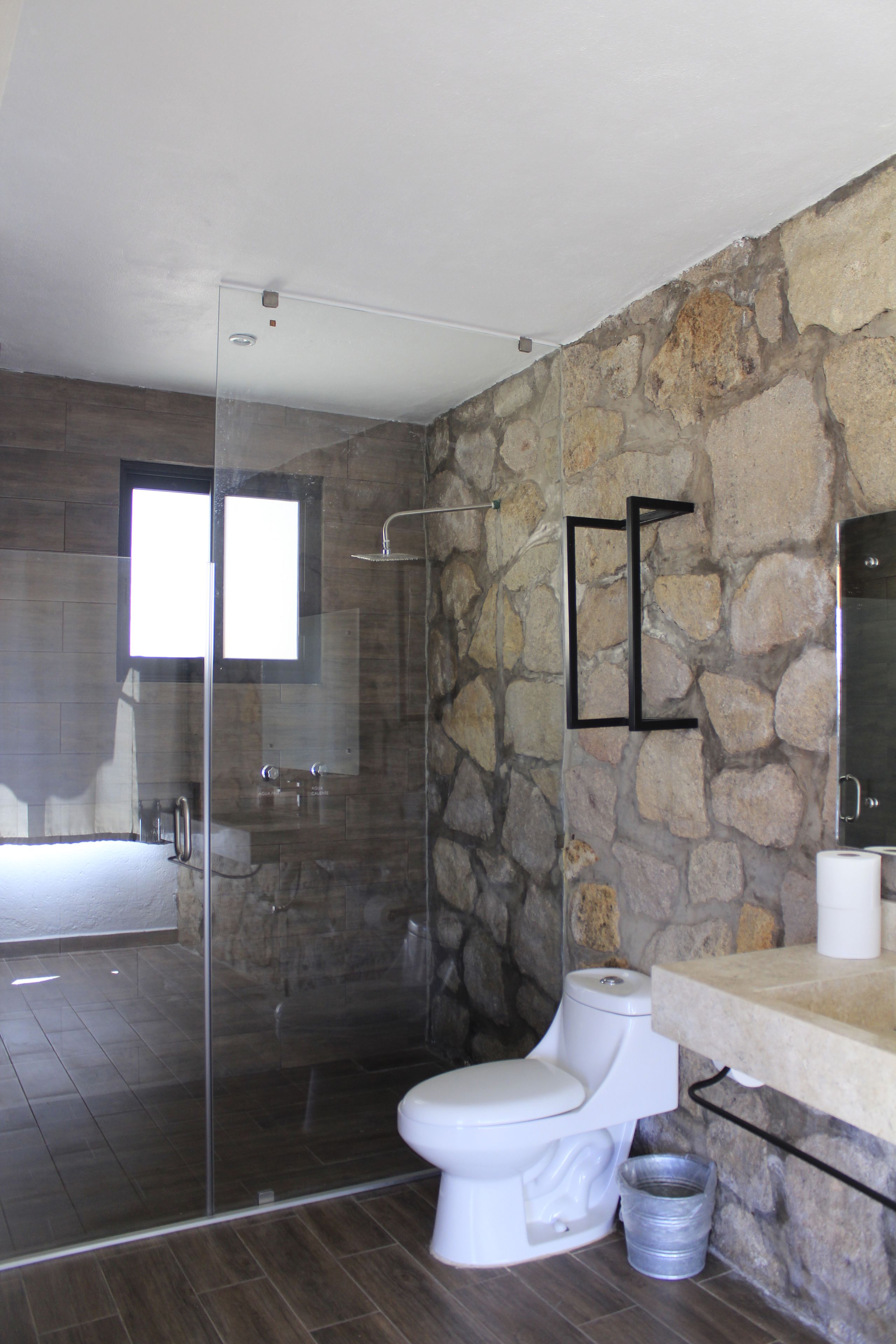Un baño moderno con pared de piedra, cabina de ducha de vidrio, inodoro y lavabo.