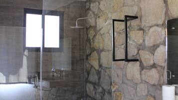 Un baño moderno con pared de piedra, cabina de ducha de vidrio, inodoro y lavabo.