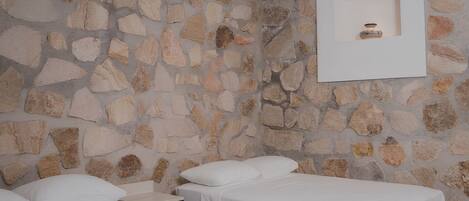A room with a stone wall, two beds, a nightstand, and a framed picture on the wall.