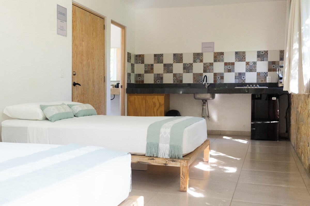 Una habitación con una cama, un pequeño rincón de cocina y la puerta de un baño.