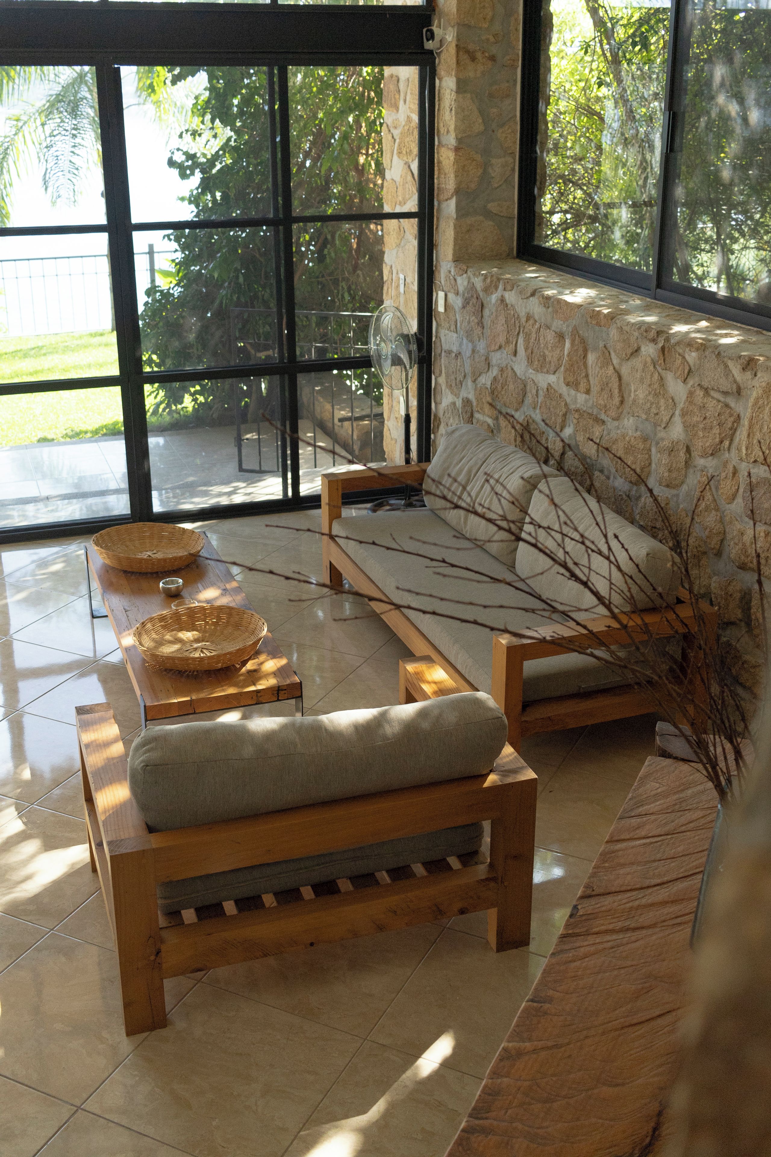 A modern living room with a stone wall, a wooden sofa, and a glass door leading to an outdoor area.