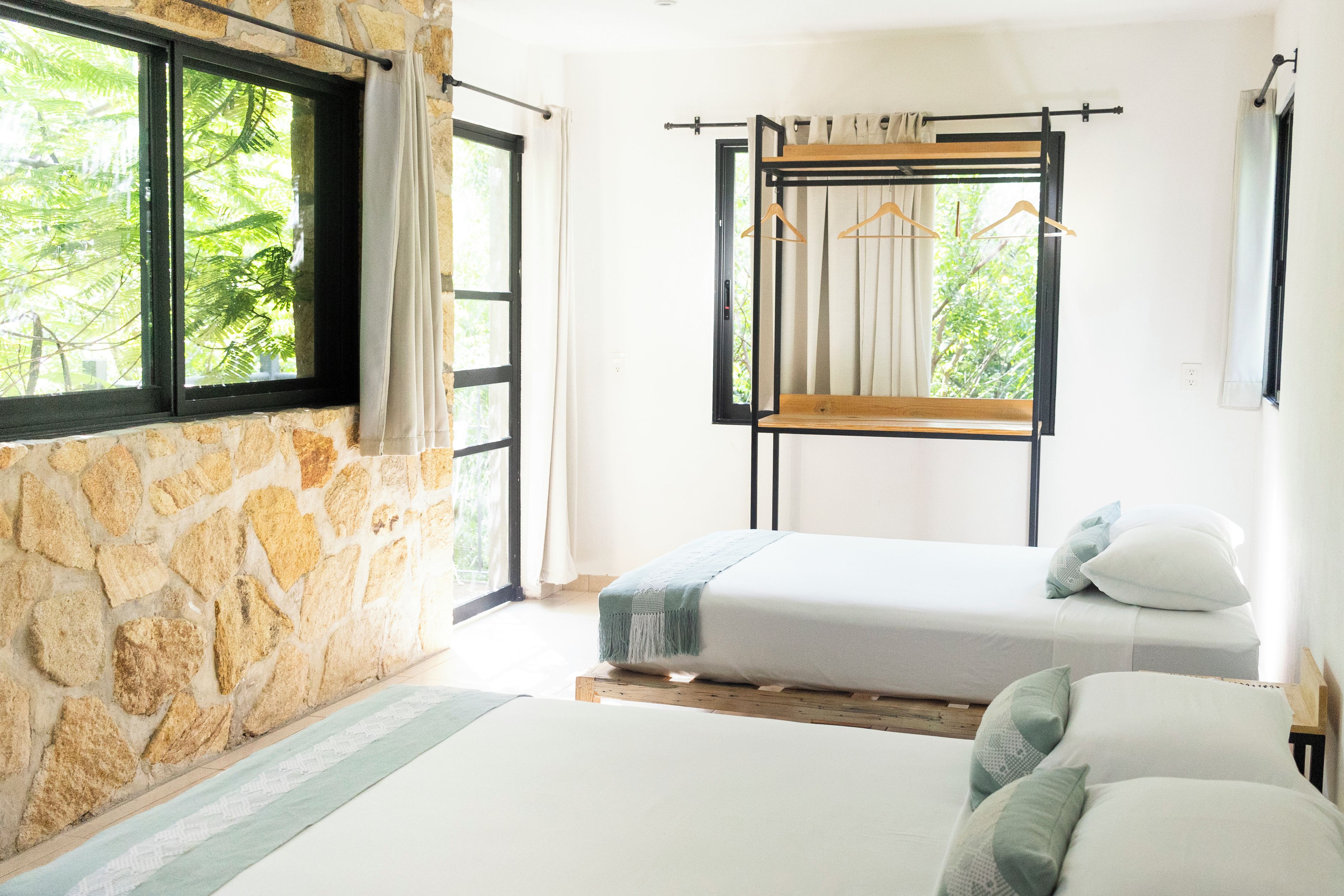 A room with two beds, a stone wall, and a window with a view of greenery.