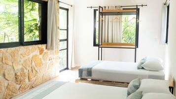 A room with two beds, a stone wall, and a window with a view of greenery.
