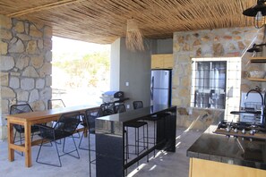 Una cocina con pared de piedra, una mesa de madera con sillas, un refrigerador y una parrilla.